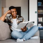 African man resting on his couch reading a book