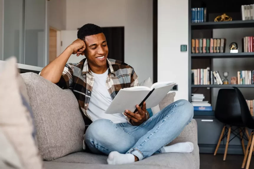 African man resting on his couch reading a book